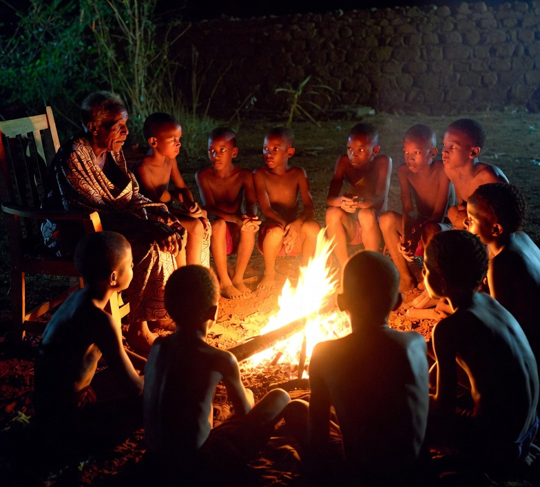 Elder sharing a story with children around a fire.